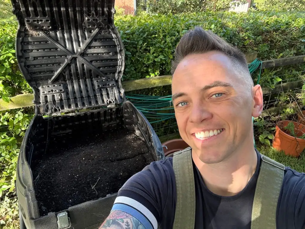 Lee Burkhill smiling in front of an open compost tumbler full of finished compost
