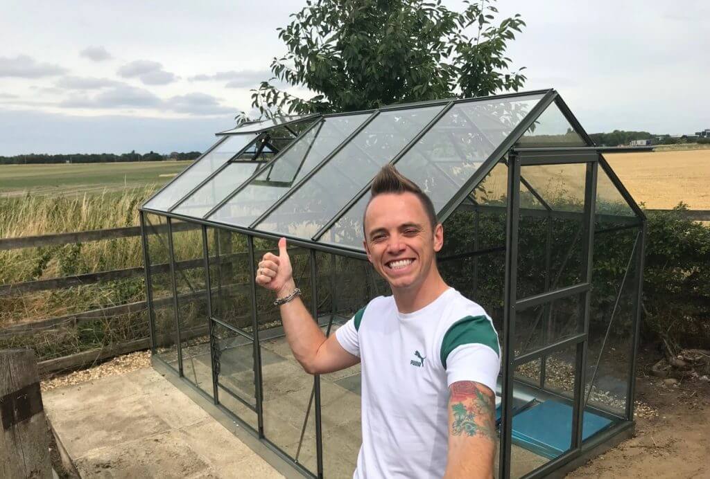 Garden Blogger Lee Burkhill pointing at a greenhouse