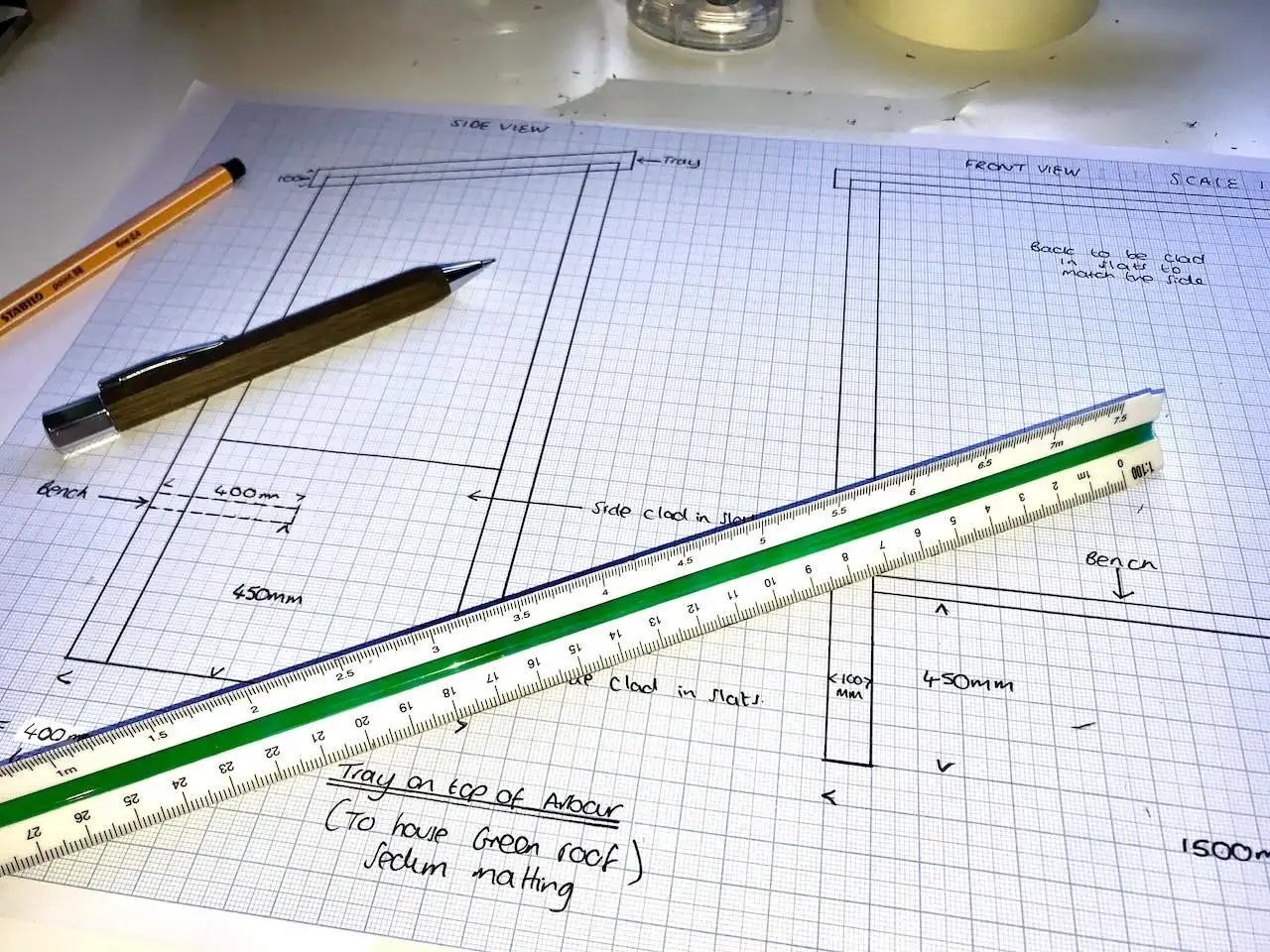 A three-sided architect's scale ruler resting on a hand drawn garden design