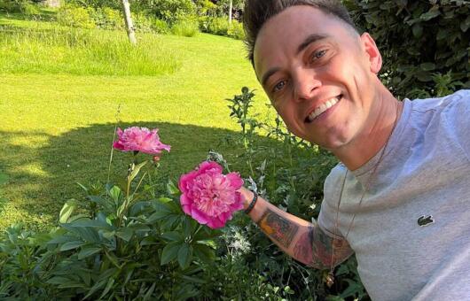 Lee Burkhill holding a bunch of pink Peonies beside a lawn and flower bed